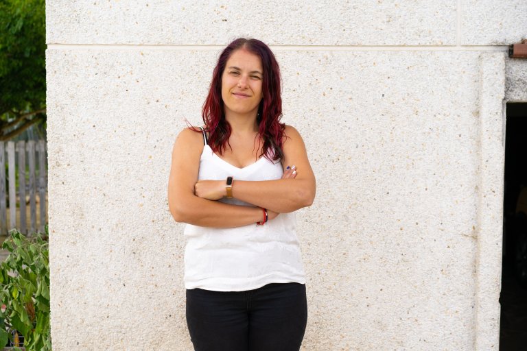 Photo of Raquel, arms folded against a white wall.